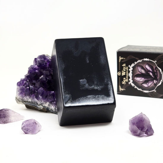 Roque Grooming Soap, slightly wet, resting against an amethyst. Its packaging rests in the background.