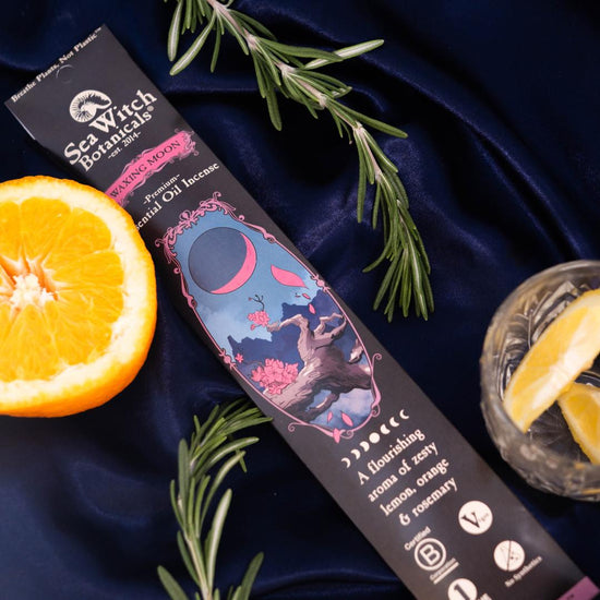 Sea Witch Remedies product packaging on a dark blue fabric background with an orange and rosemary.