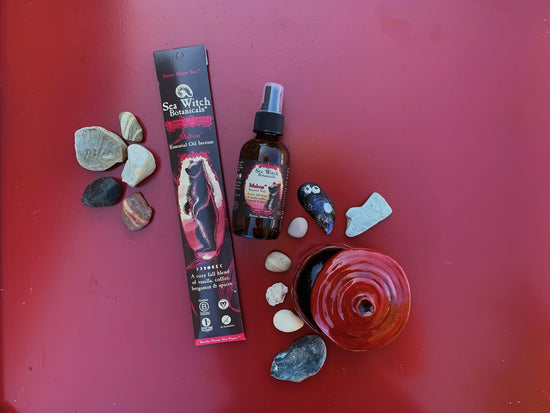 Sea Witch Botanicals Mabon Incense and Scented Veil pictured with various stones, shells, and a small pot on a red backdrop.