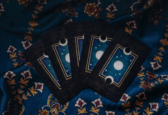 Black and blue tarot card with moons lying facedown on an ornate sheet with yellow and red designs on a blue backdrop