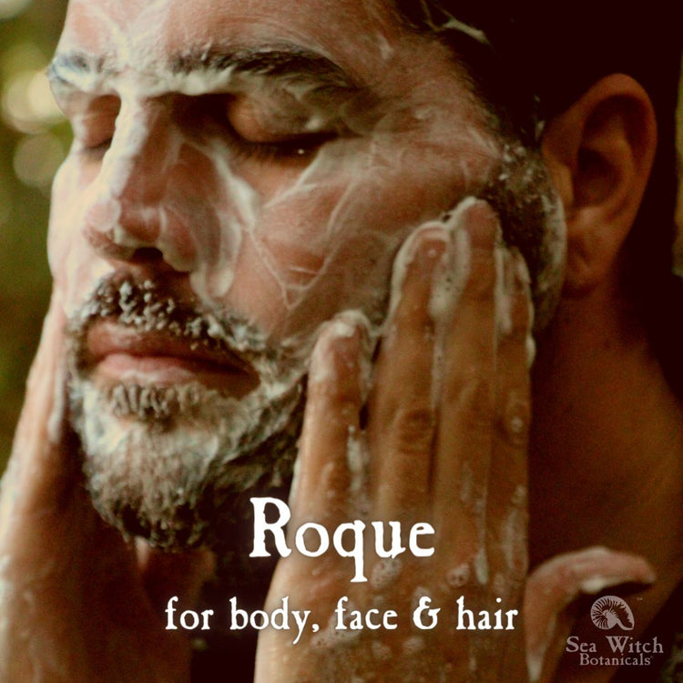 A man with a short dark beard washes his face with Roque grooming soap. Text reads "Roque: for body, face & hair"