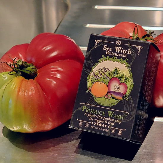 Box of produce wash with two heirloom tomatoes on a stainless steel sink