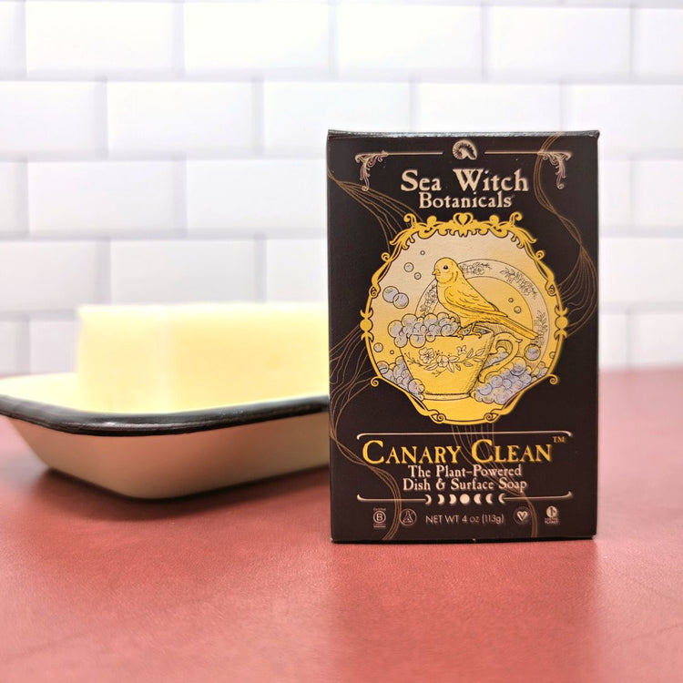 Canary Clean in a box stands on a red countertop with white backsplash in front of a soap dish holding a bare bar.