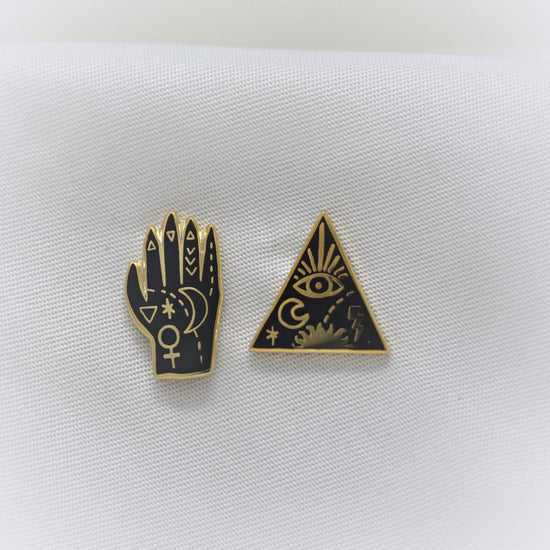 Yellow Owl Workshop Earrings - Mystic Powers. One is a palm-reading-style hand and the other is an all seeing eye triangle with extra flair.