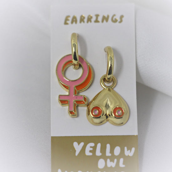 Yellow Owl Workshop Drop Charm Earrings - One is a pink female symbol, the other is a pair of gold breasts with pink nipples.
