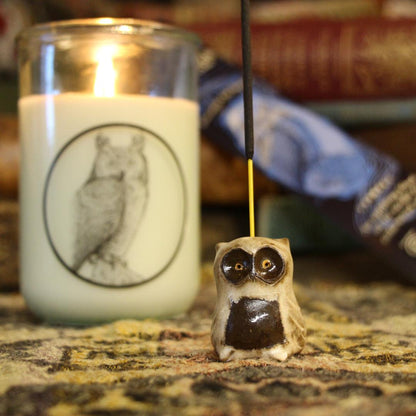 Brown Owl clay incense holder on a table with books and a burning candle in the background.