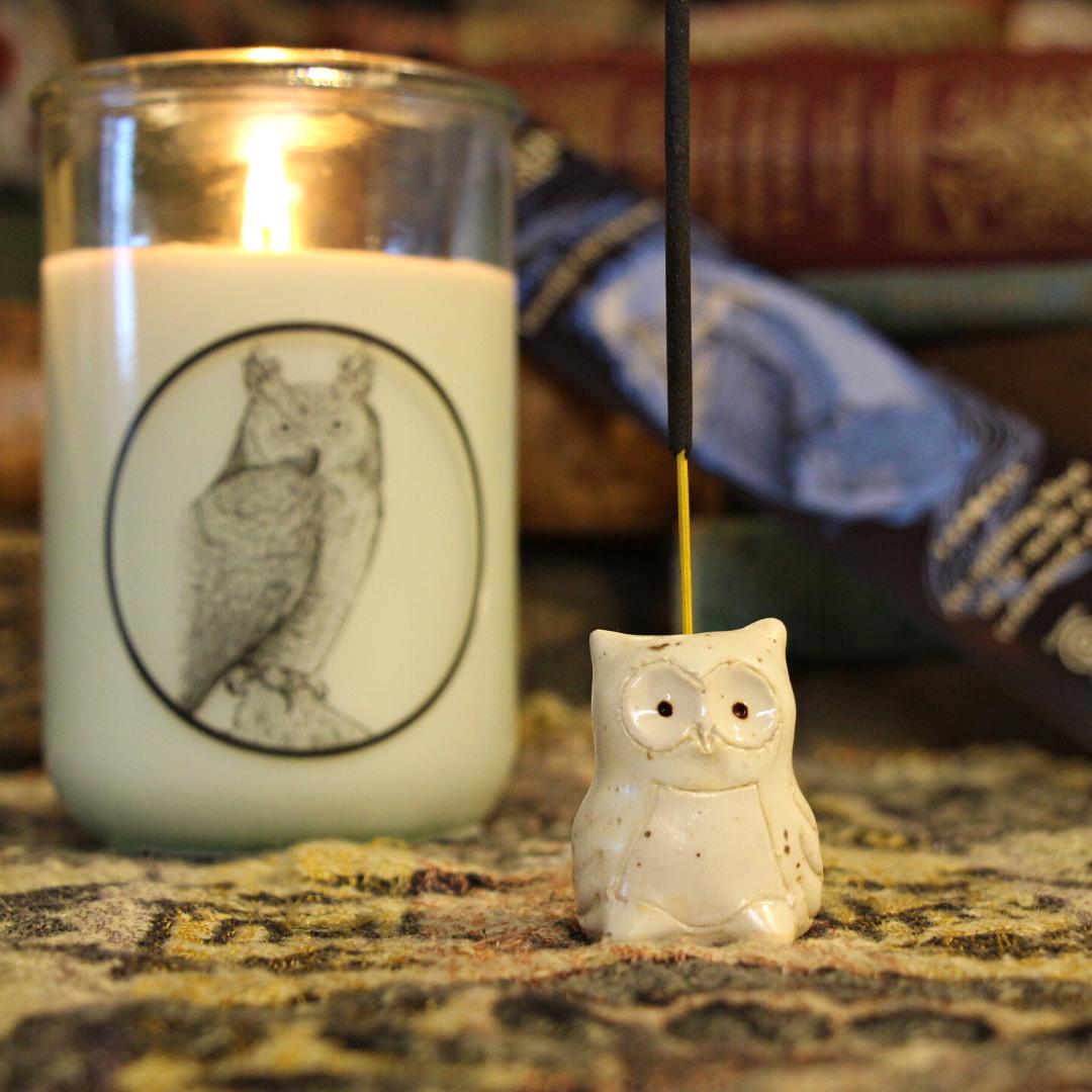 Snowy Owl clay incense holder on a table with books and a burning candle in the background. 