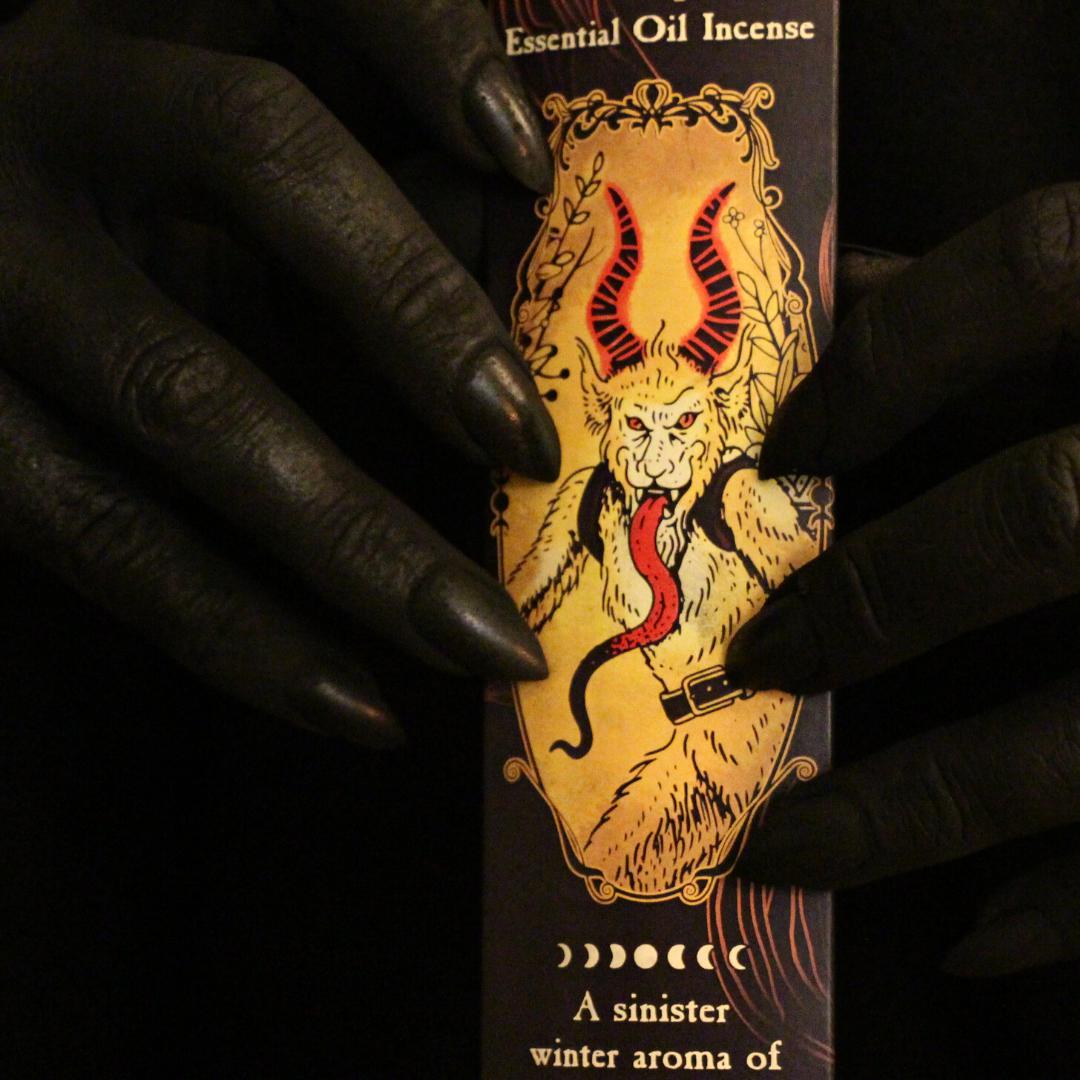 soot-black hands with claw nails holding a 20 pack of Krampus all natural incense