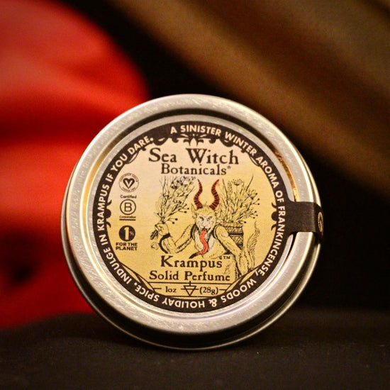 2022 limited edition Krampus solid perfume in recyclable tin on a black set with red and gold fabrics in the background