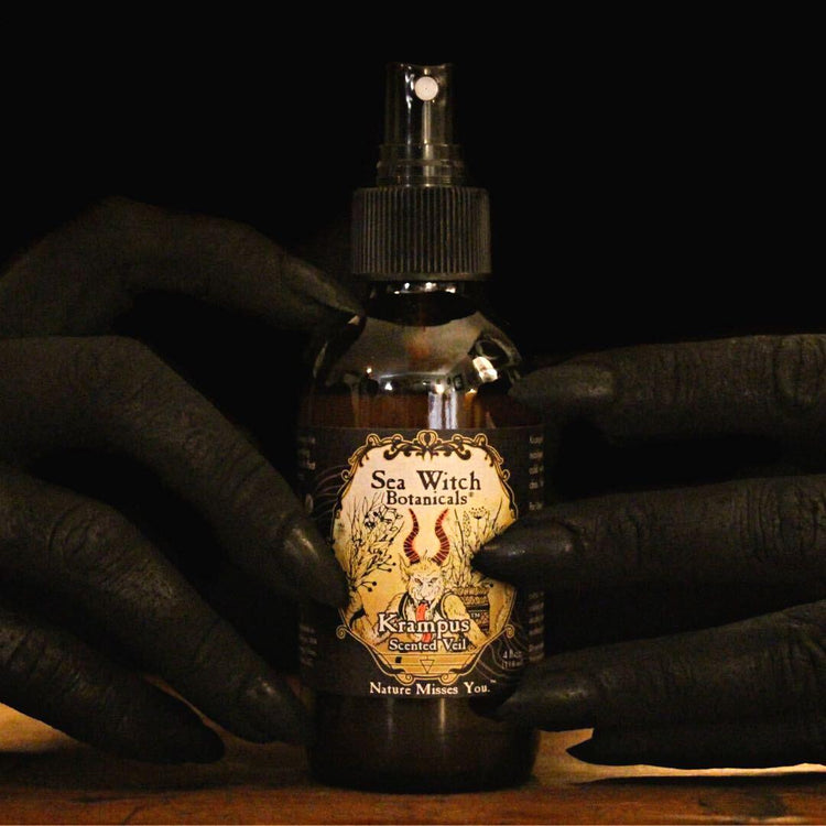 Soot-black hands with claw-like nails around a bottle of limited edition Krampus essential oil scented veil and room spray.