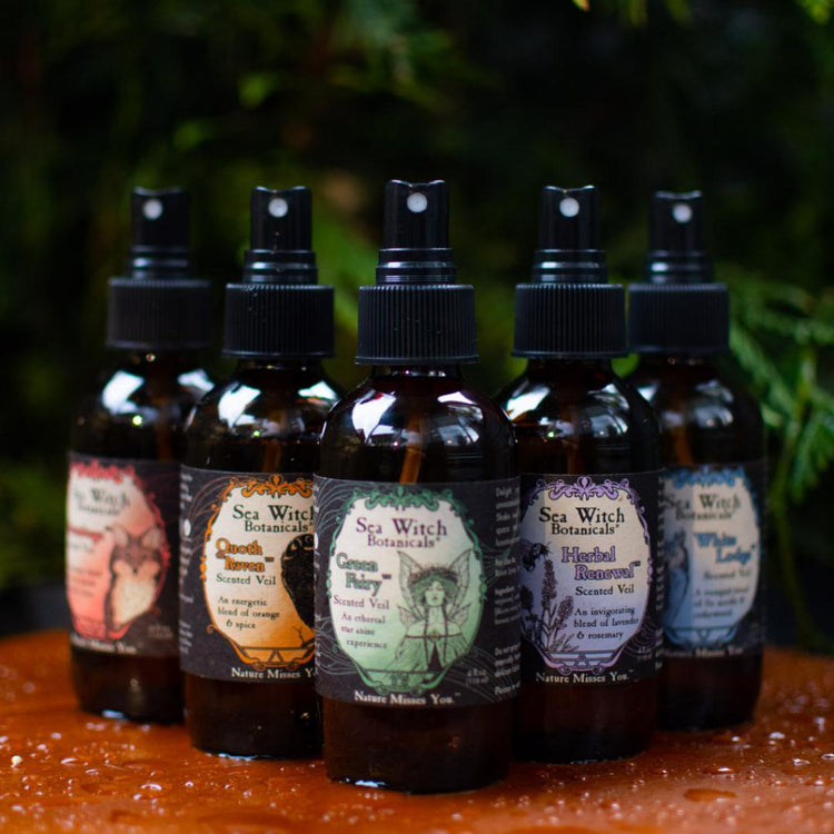 Sea Witch Botanicals Scented Veil Essential Oil Spray Perfume Collection on wet wood in front of fir trees